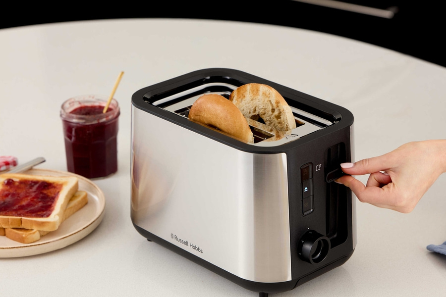 Ein Toaster mit Brot, daneben Marmelade und Toast auf einem Teller.
