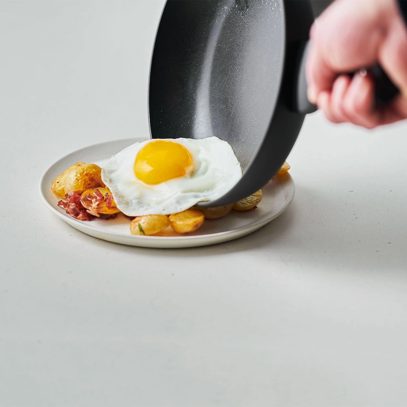 Ein Teller mit Spiegelei, Kartoffeln und Speck, serviert mit einer Pfanne.