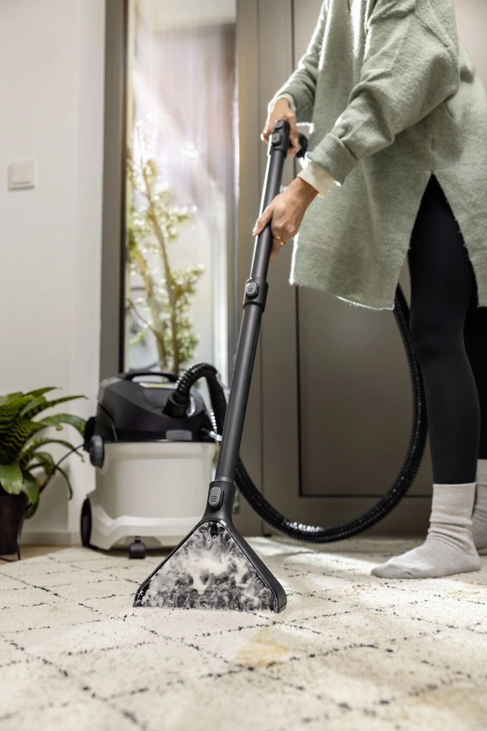 Frau reinigt Teppich mit einem Waschsauger.
