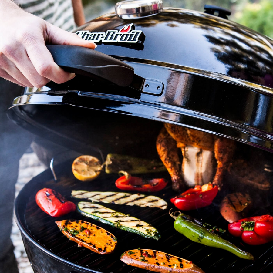 Grill mit Gemüse und Hähnchen. Person öffnet den Deckel.