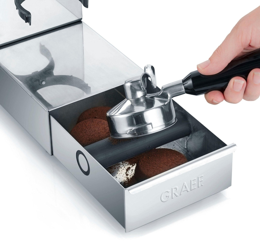 Edelstahl-Kaffeemaschine mit Schublade und Kaffeesatz. Person hält Siebträger.