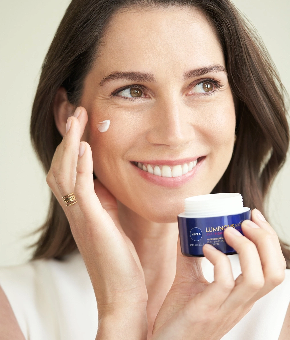 Frau trägt Creme auf, hält Cremebehälter, lächelt, Nahaufnahme, Nivea Luminous 630