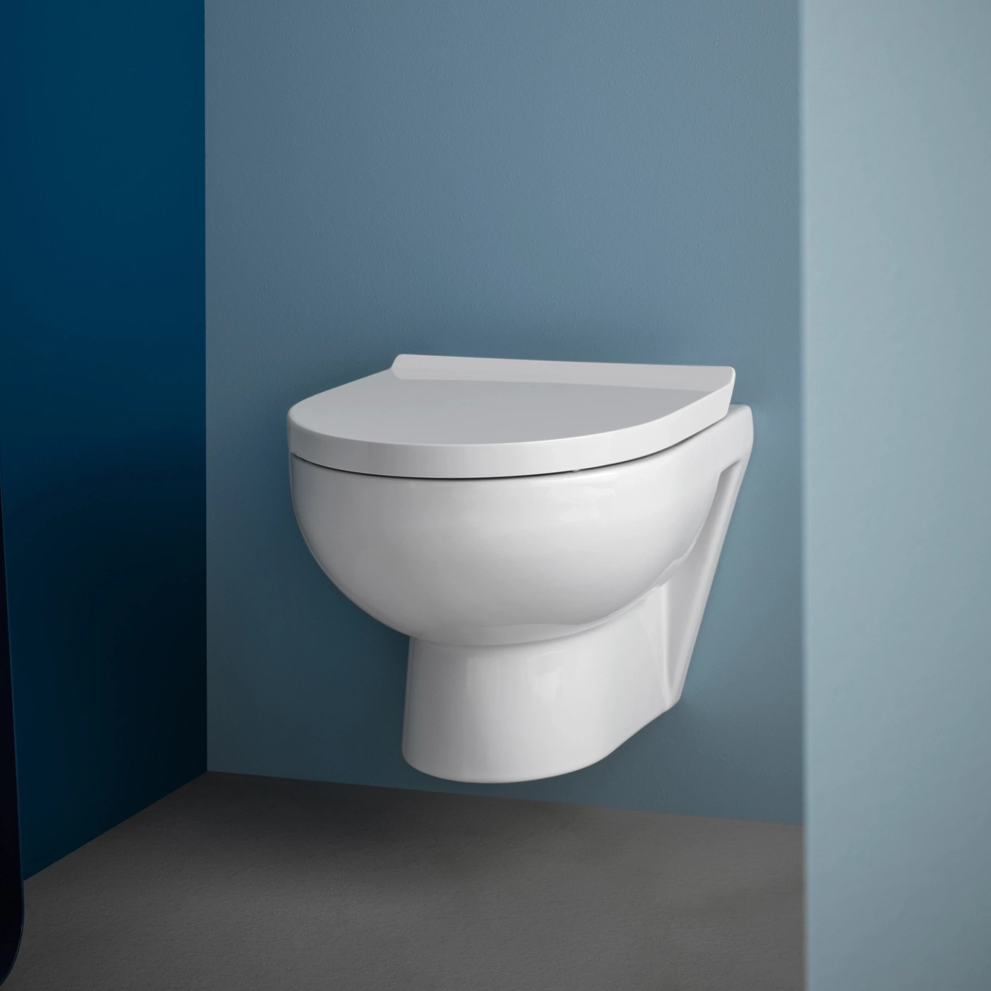 Eine weiße Wandtoilette hängt an einer blauen Wand. Der Boden ist dunkelgrau.