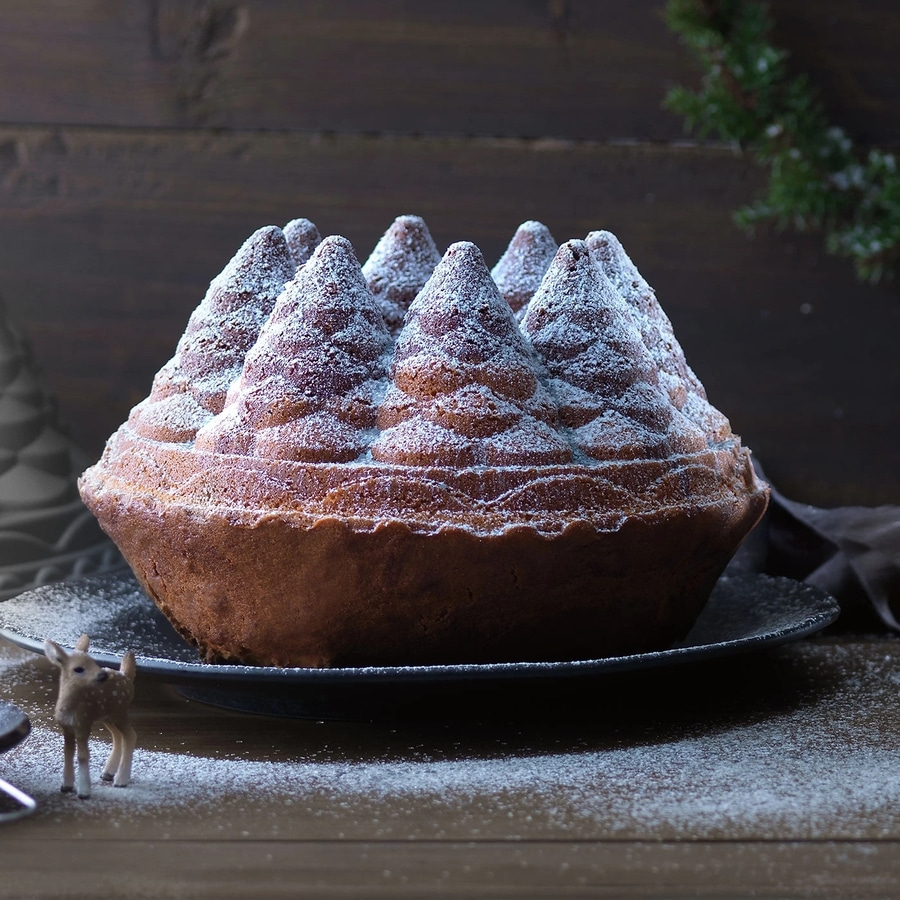 Ein Kuchen in Form eines Weihnachtsbaums, mit Puderzucker bestäubt, auf einem Teller.