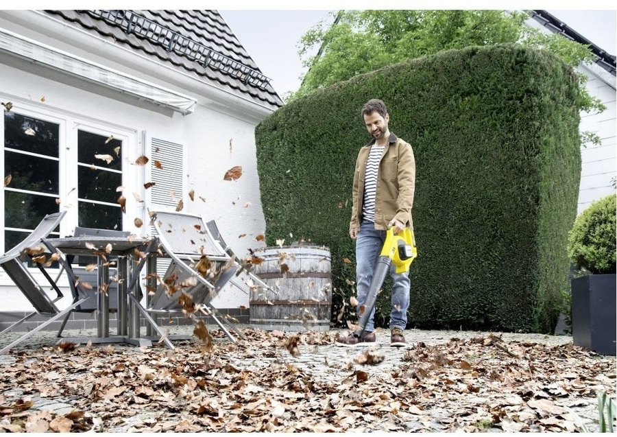 Mann bläst Blätter mit einem Laubbläser im Garten weg. Herbstliche Gartenarbeit.