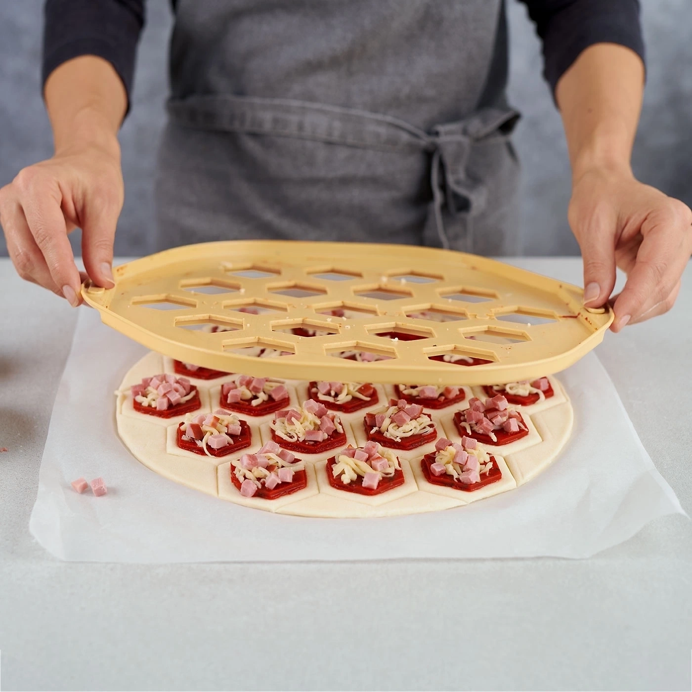 Person hält Werkzeug über Pizza mit Belag, um sie zu formen.
