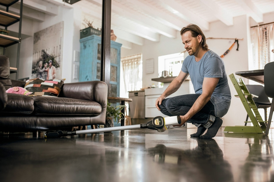 Mann saugt Boden vor braunem Ledersofa mit Staubsauger