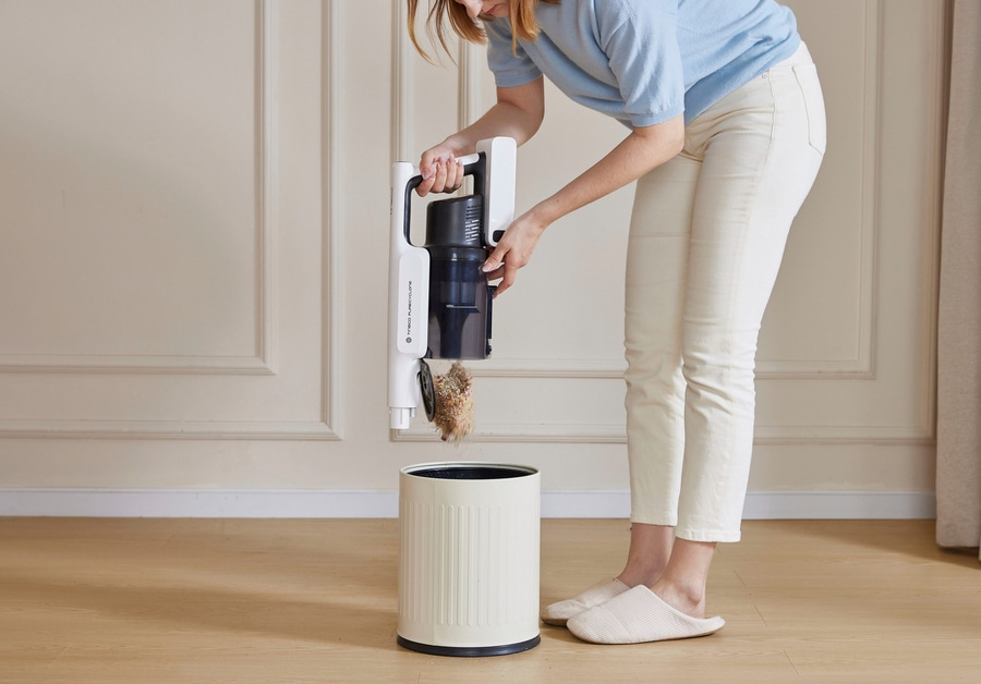 Frau entleert Staubsauger in einen Mülleimer, um Haus sauber zu machen.