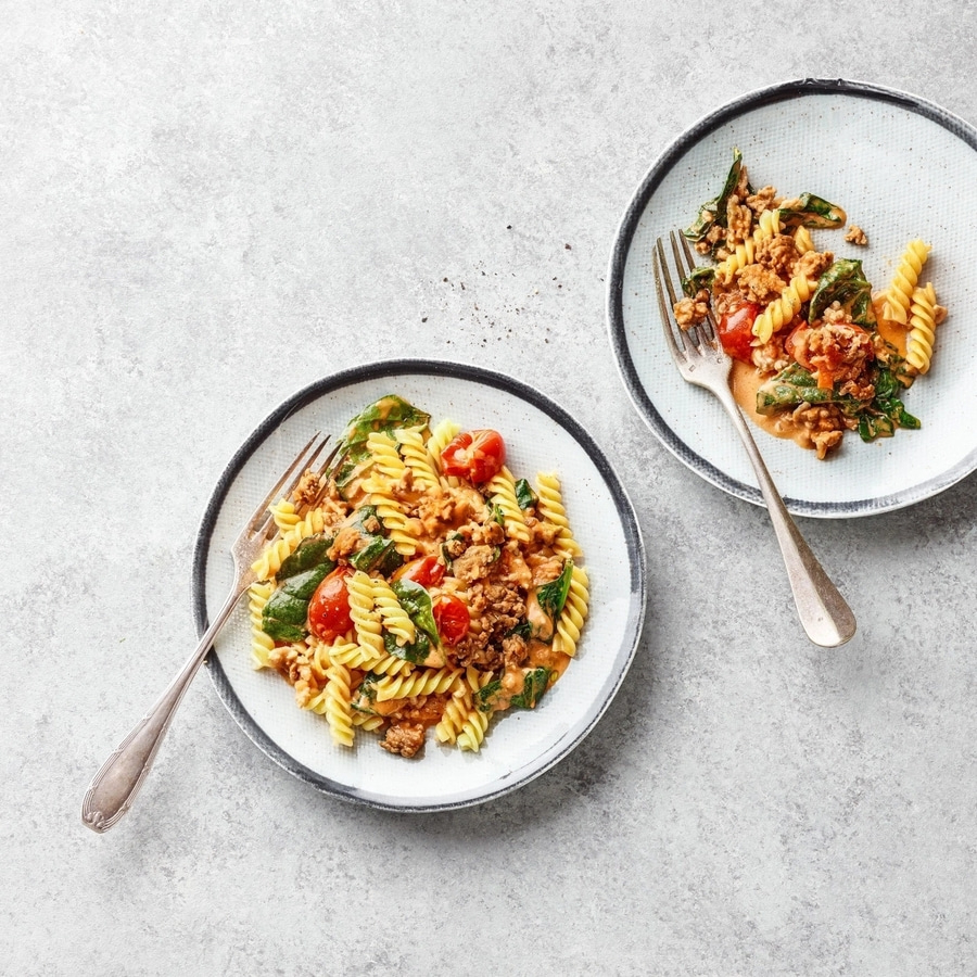 Zwei Teller Pasta mit Fleisch, Tomaten und Spinat auf grauem Hintergrund