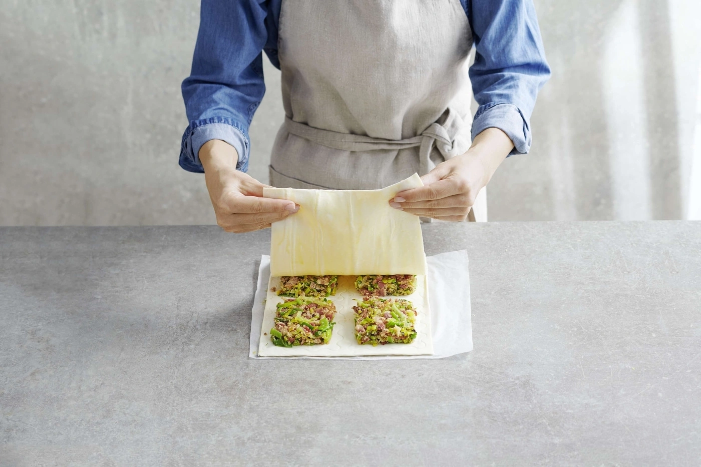 Person legt Teig auf gefüllte Quadrate auf einem Tisch. Kochen, Essen, Küche.