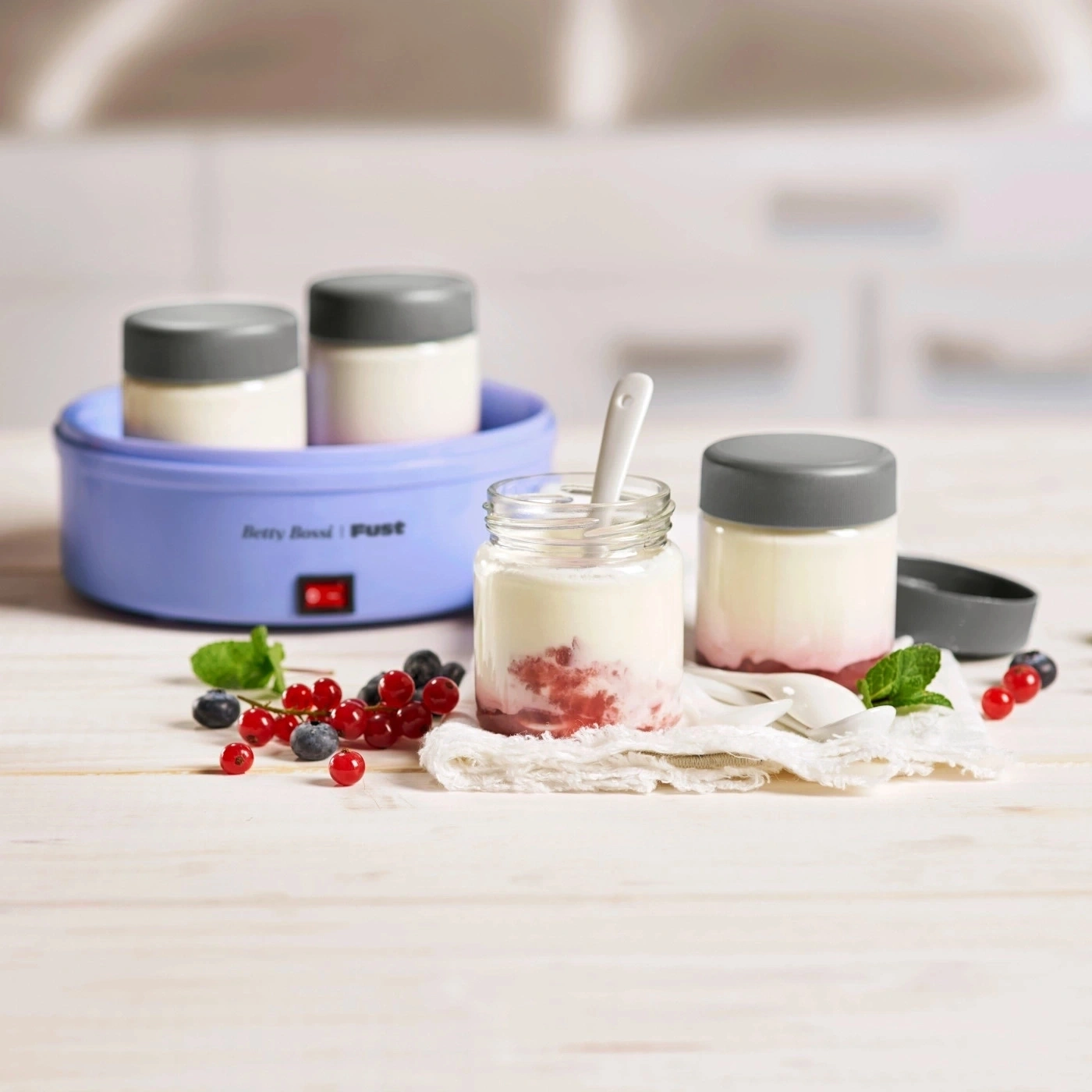 Joghurtgläser mit Beeren und Minze auf Holzoberfläche mit Joghurtbereiter