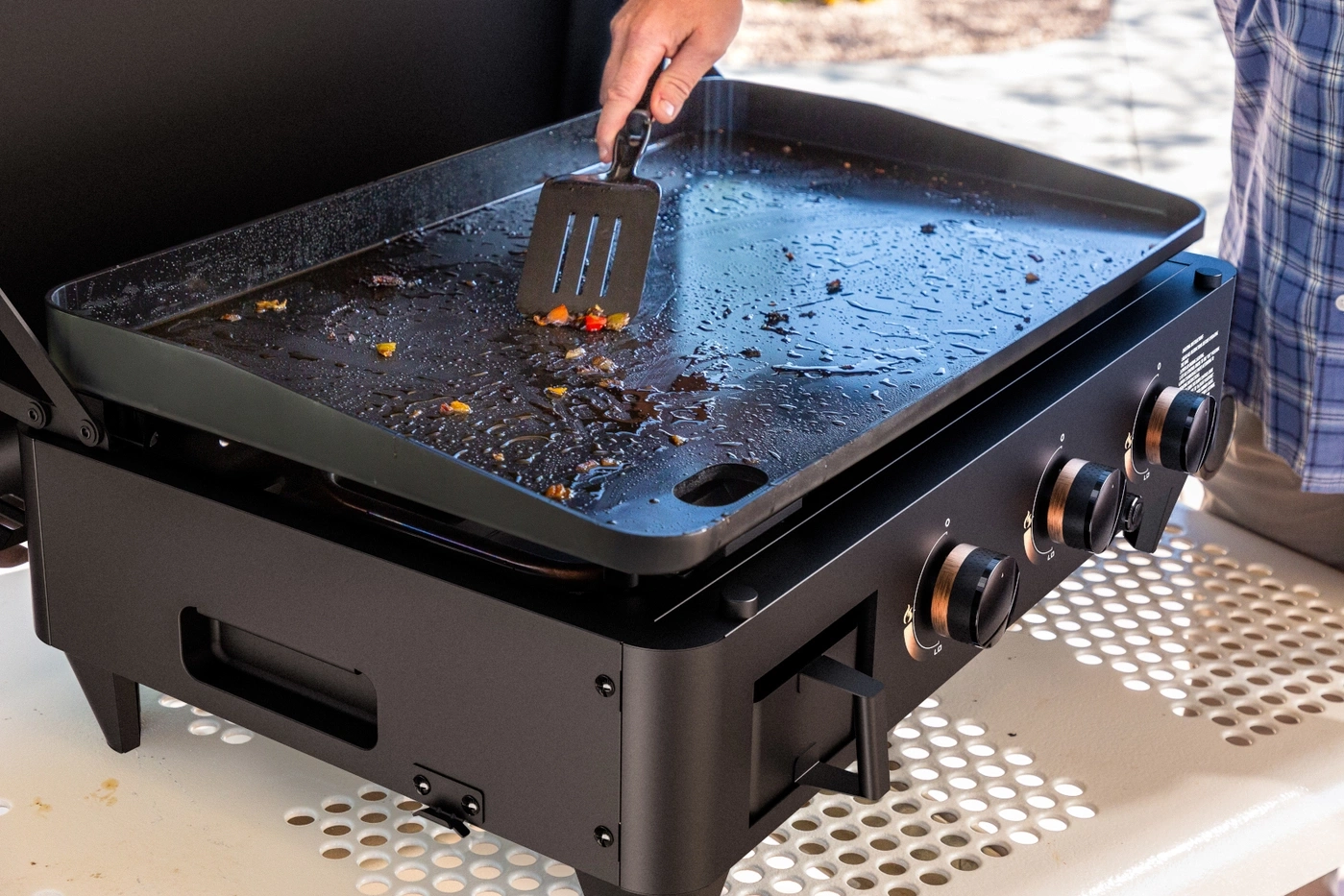 Eine Person reinigt eine heiße Grillplatte mit einem Spatel.
