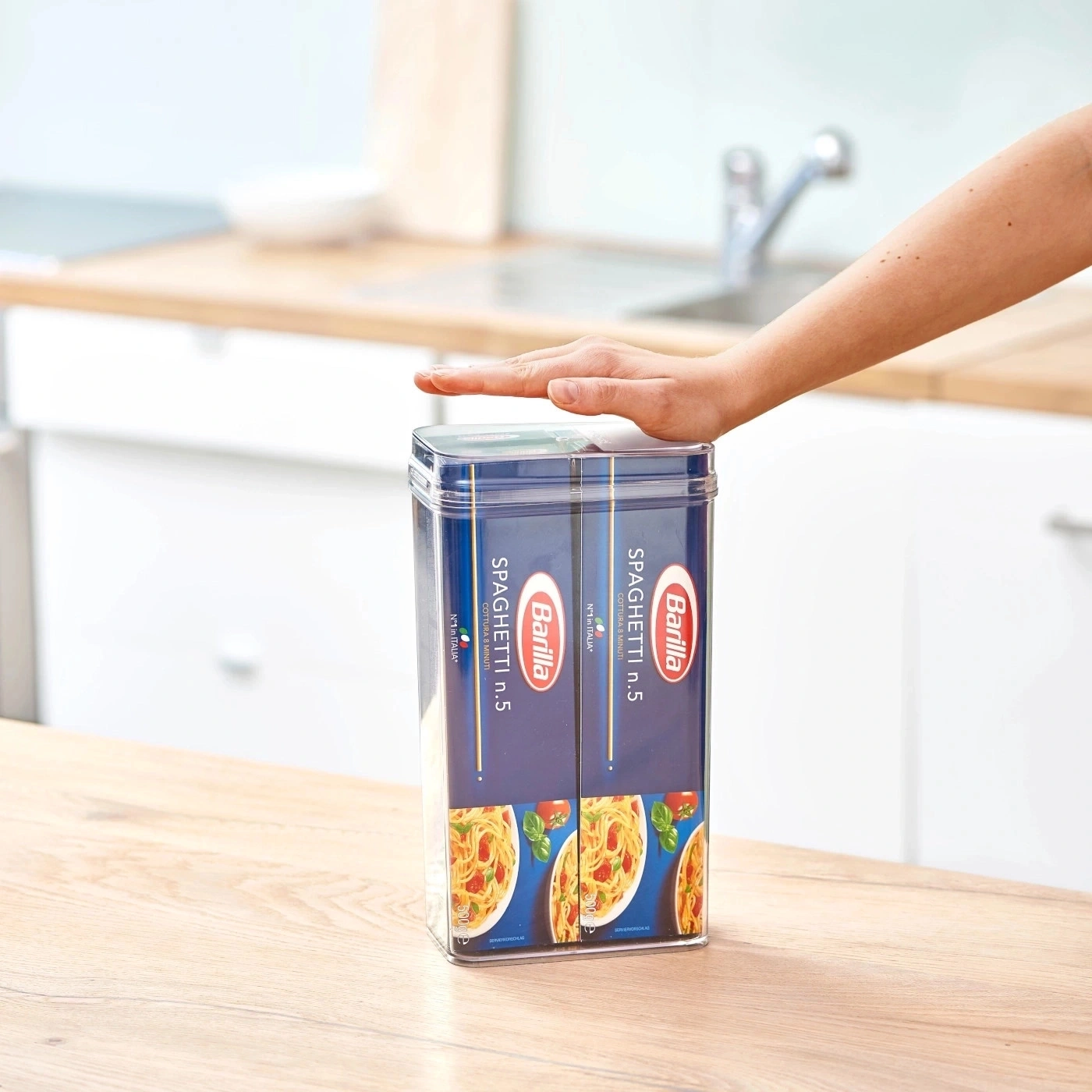 Person berührt Spaghetti-Packungen auf einem Holztisch in der Küche.