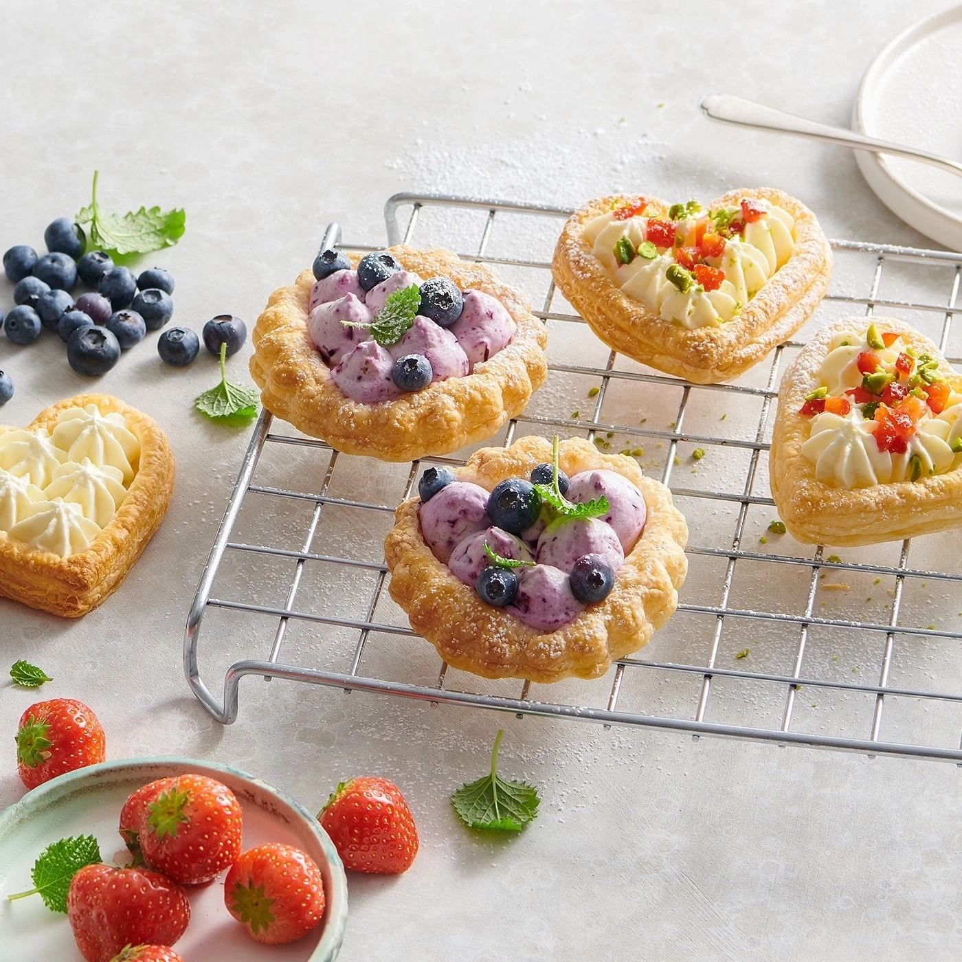 Gebäck mit Blaubeeren und Sahne auf einem Rost, Erdbeeren daneben
