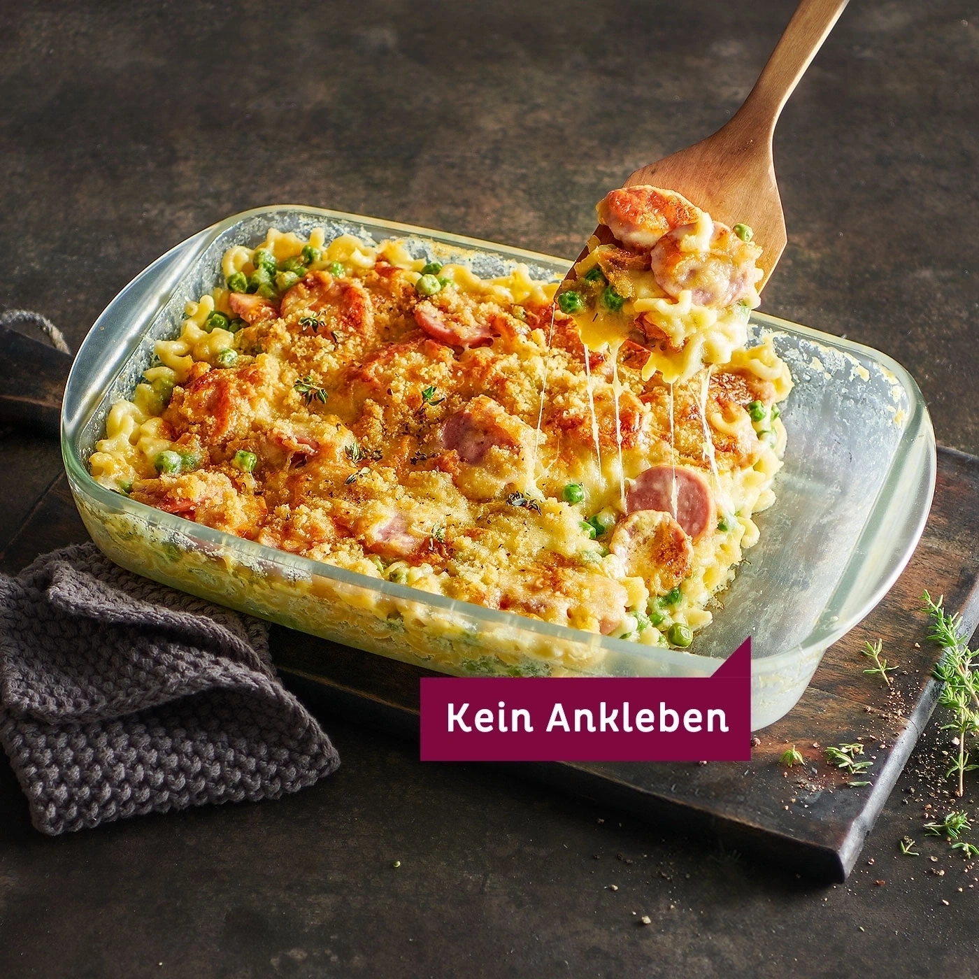 Auflauf mit Wurst, Erbsen und Käse, serviert mit einem Holzspatel.